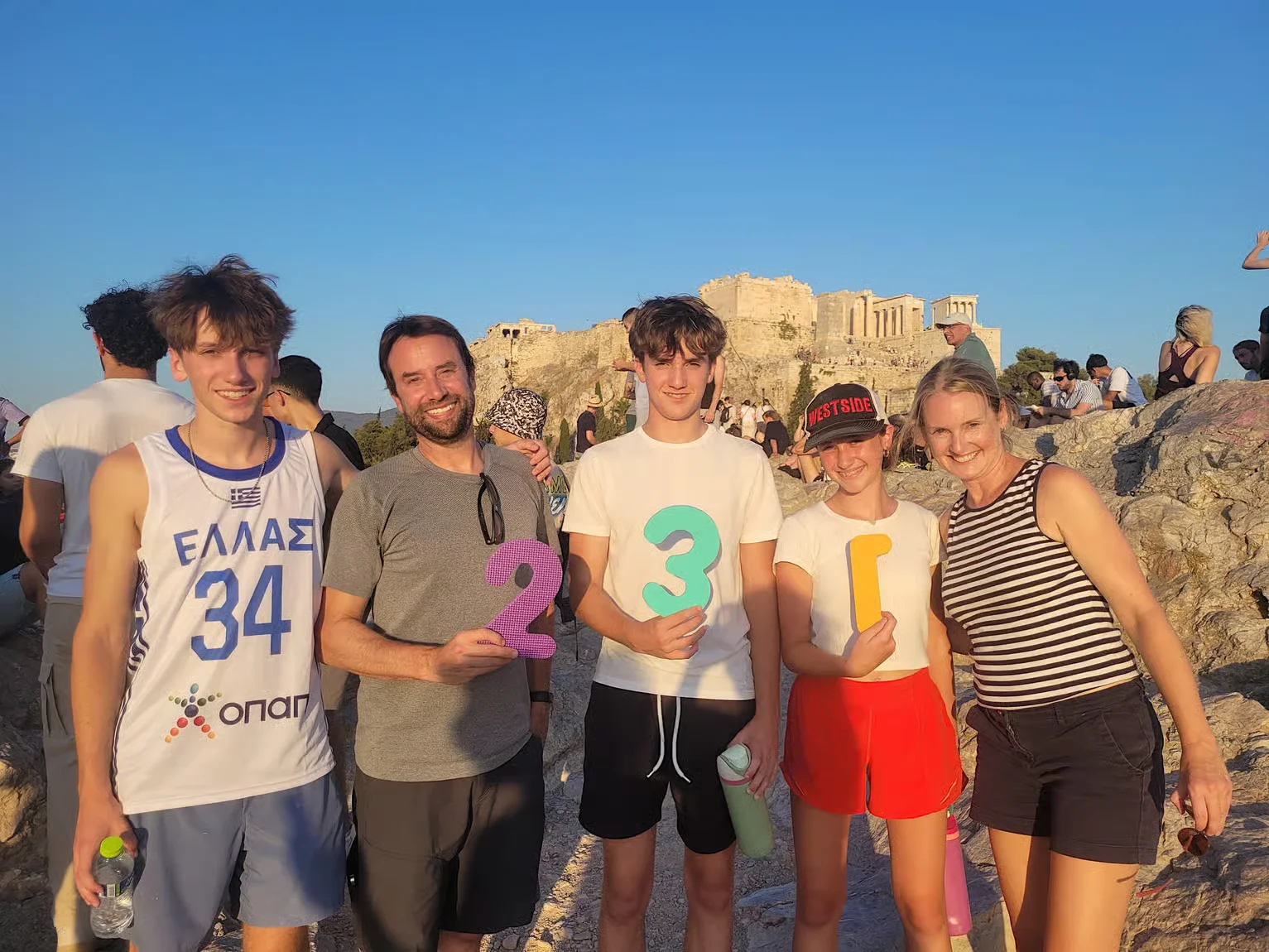 Family group smiling and holding numbers during a treasure hunt activity near the Acropolis in Athens.