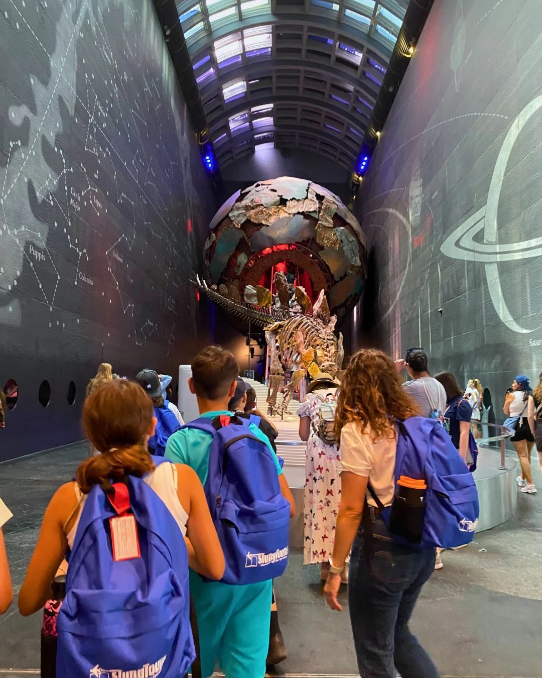 Students with backpacks exploring an interactive museum exhibit during an educational summer camp activity.